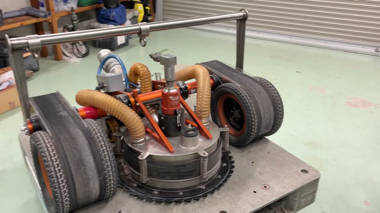 マグネットクローラーの実機。左右の車輪の間に回転ノズルのヘッドがあり、上部に吸引ホースが2本つながっている
